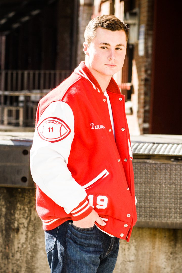 A man in red and white jacket standing on sidewalk.