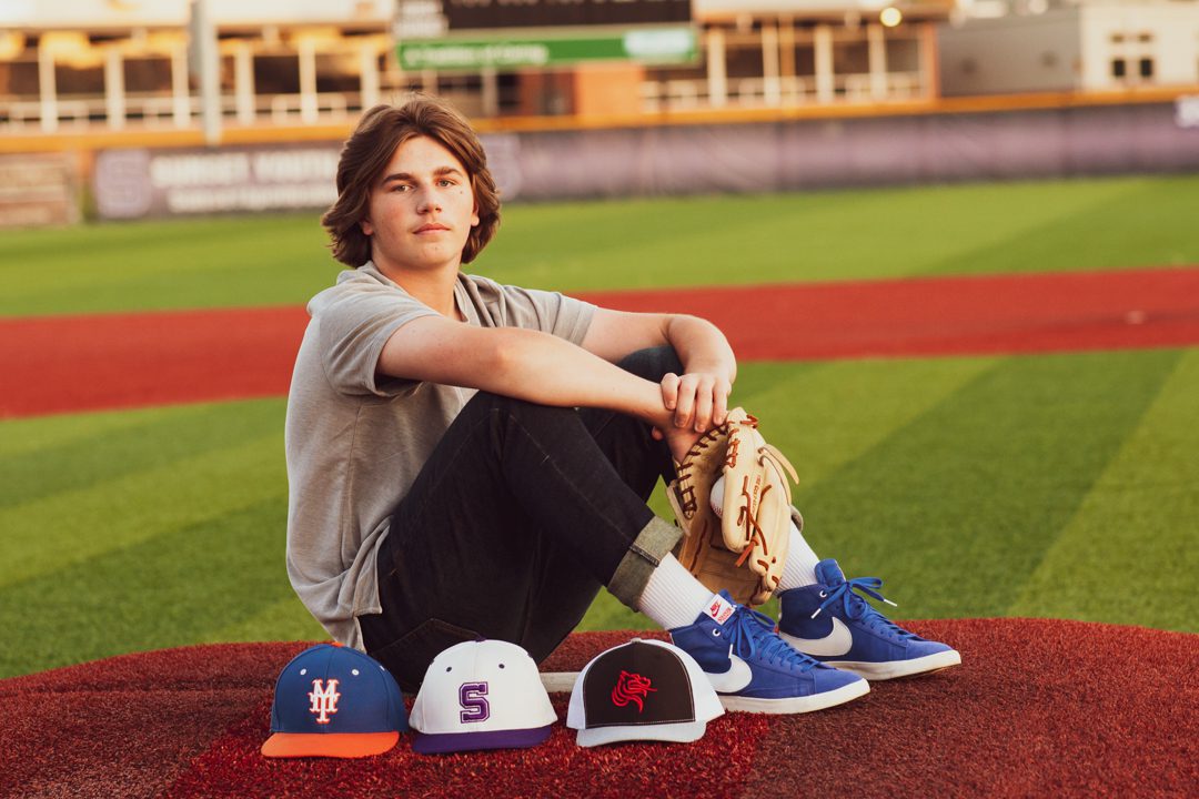 A young man sitting on the ground with his baseball gear.