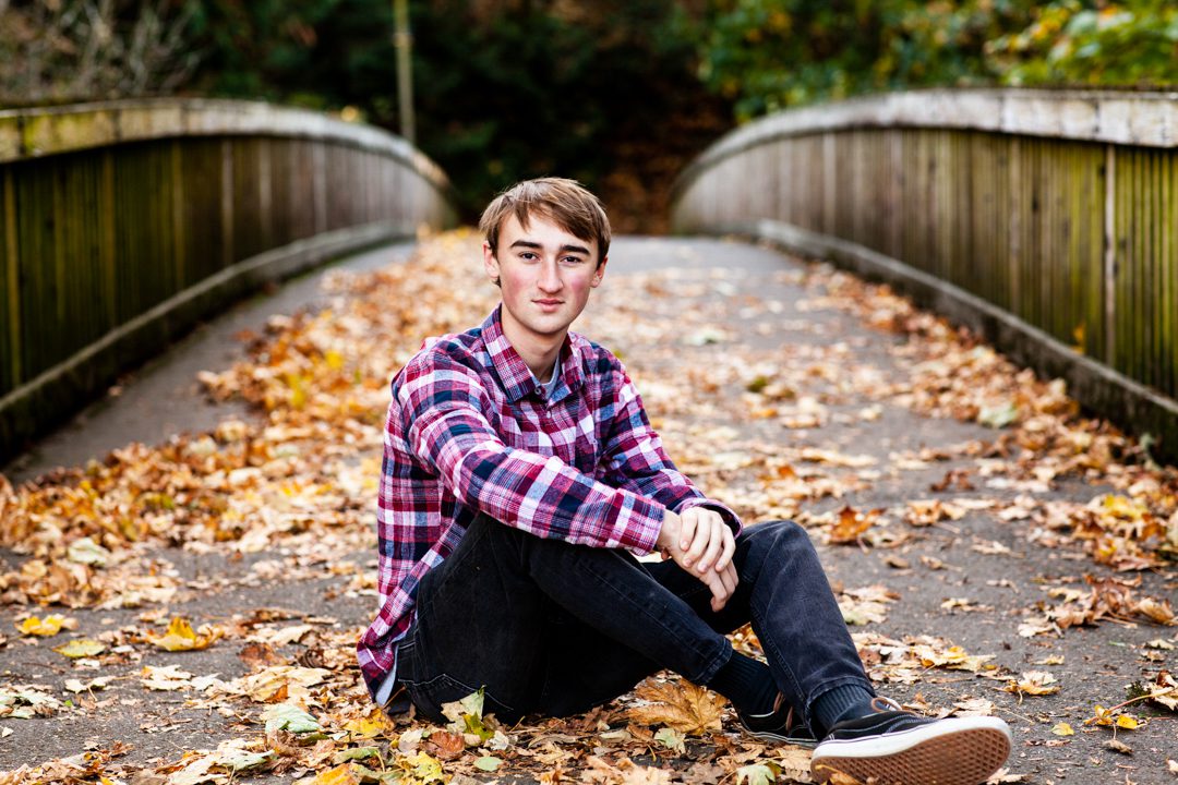 A young man sitting on the ground in front of some leaves.