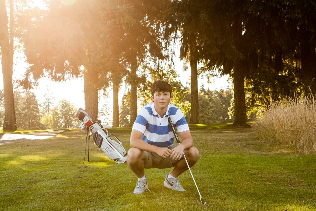 A man squatting in the grass with his golf clubs.