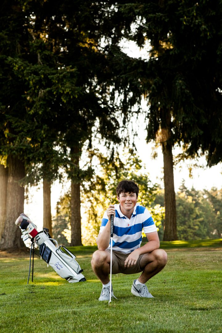 A young man kneeling down next to his golf bag.