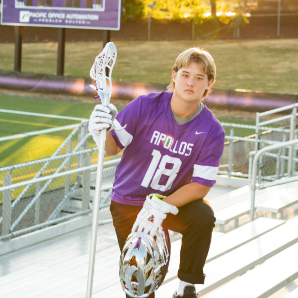A boy in purple shirt holding a lacrosse stick.