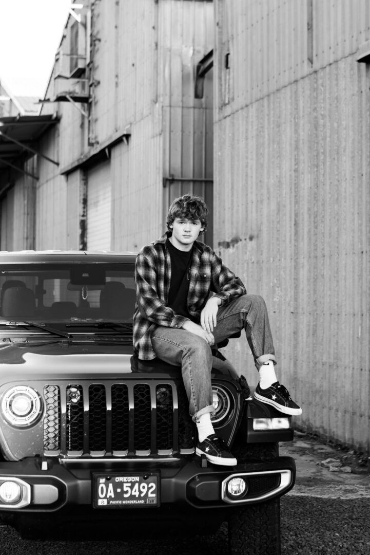 A young man sitting on the hood of a jeep.