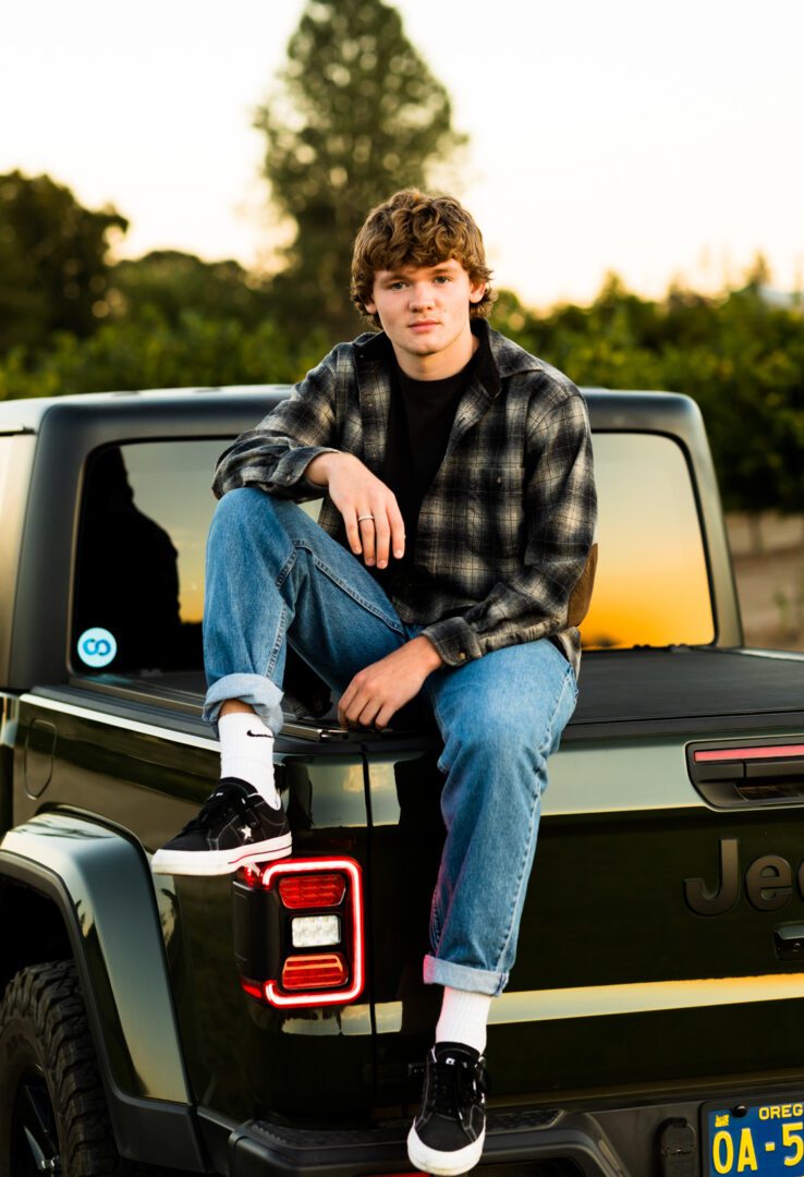 A young man sitting on the back of a truck.