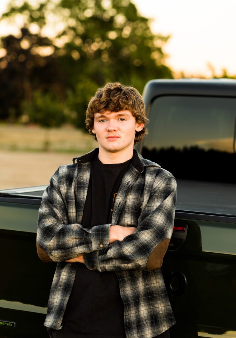 A young man standing in front of a truck.