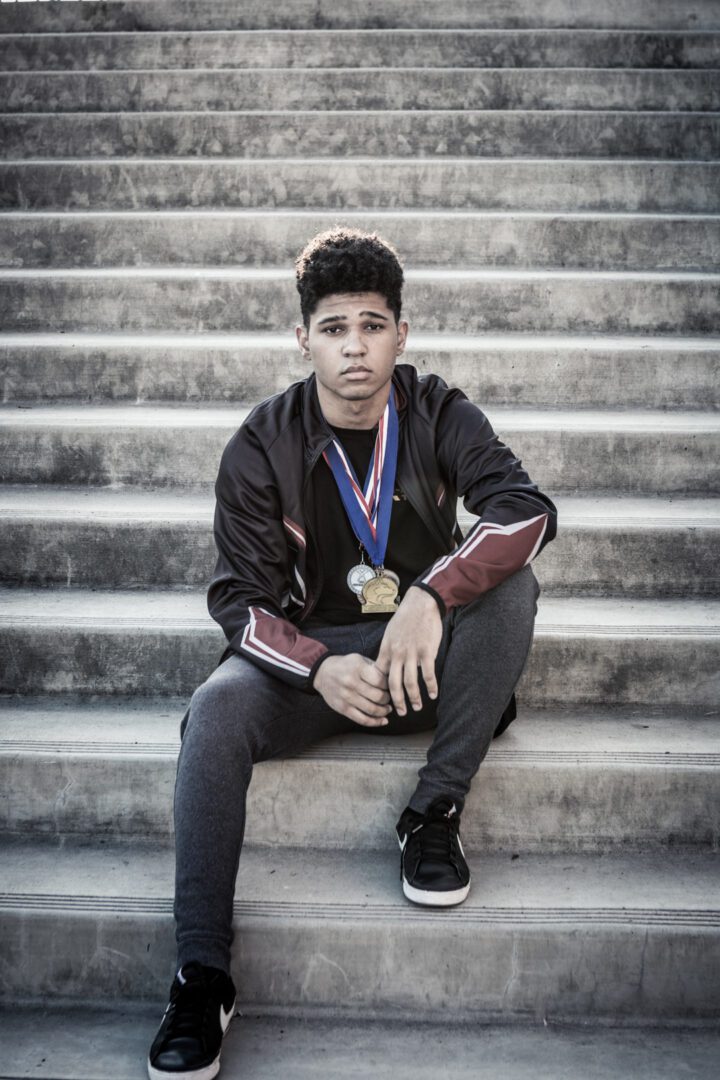 A young man sitting on some steps with medals around his neck.