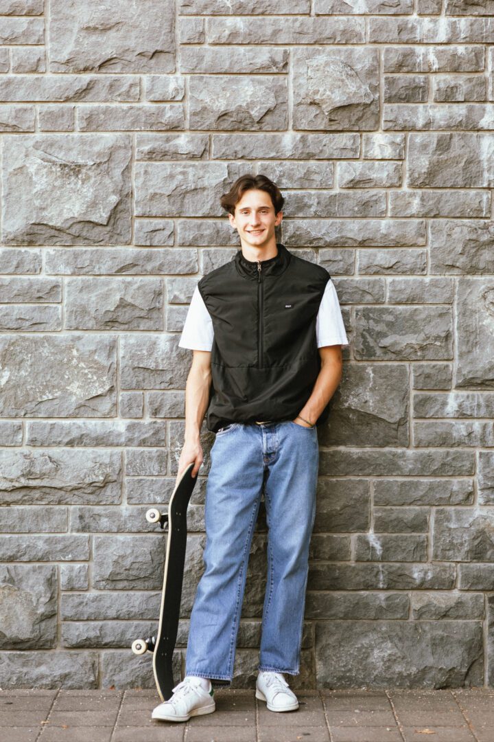 A man holding a skateboard in front of a brick wall.