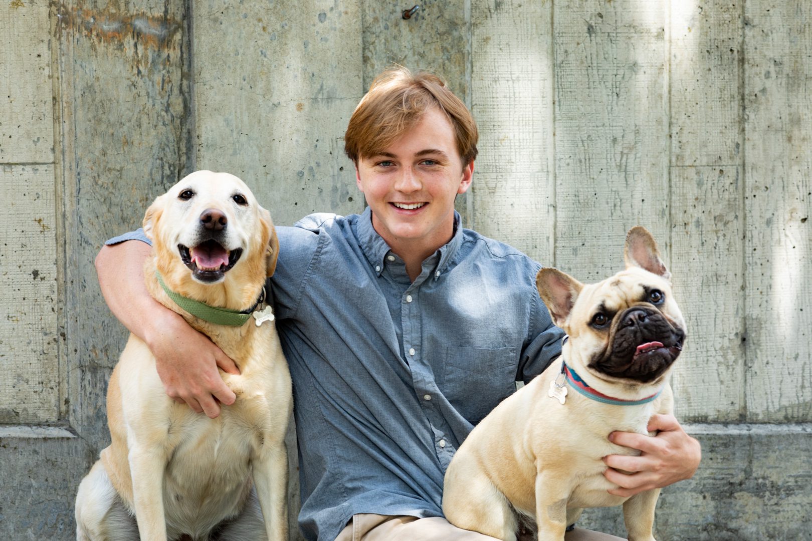 A man sitting next to two dogs in front of a wall.