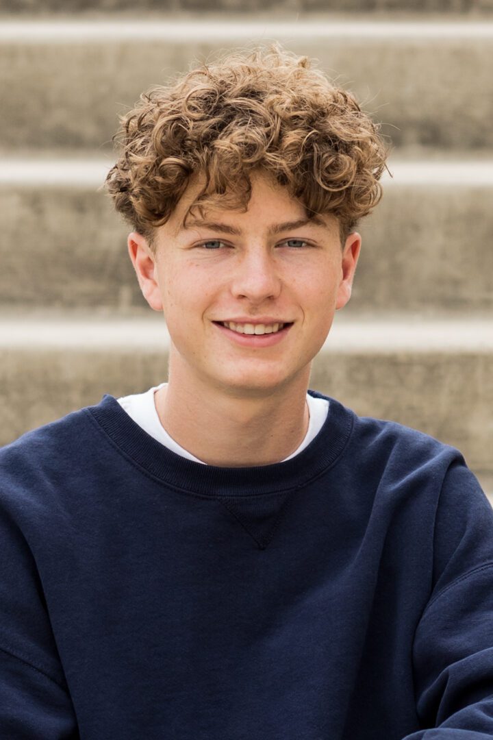 A young man with curly hair sitting on some steps.