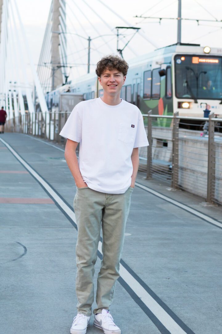 A boy standing on the sidewalk in front of a train.