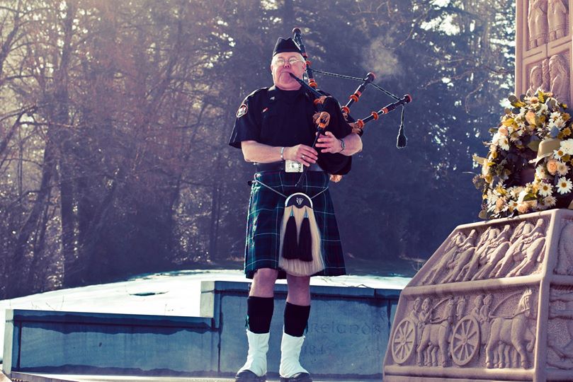 A man in black shirt playing bagpipes near trees.