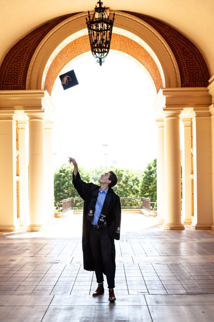 A man in a graduation gown throwing his cap into the air.