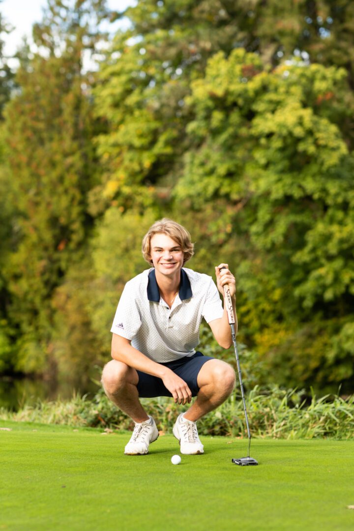 A man squatting on the grass holding a golf club.