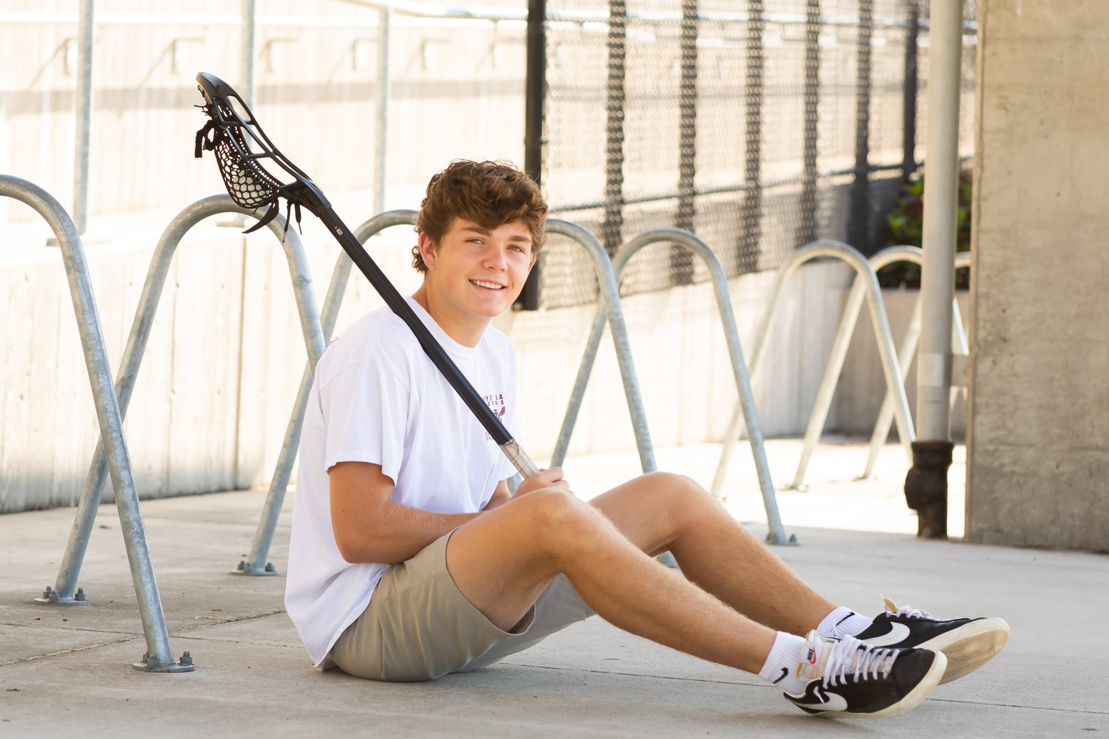 A young man sitting on the ground holding a lacrosse stick.