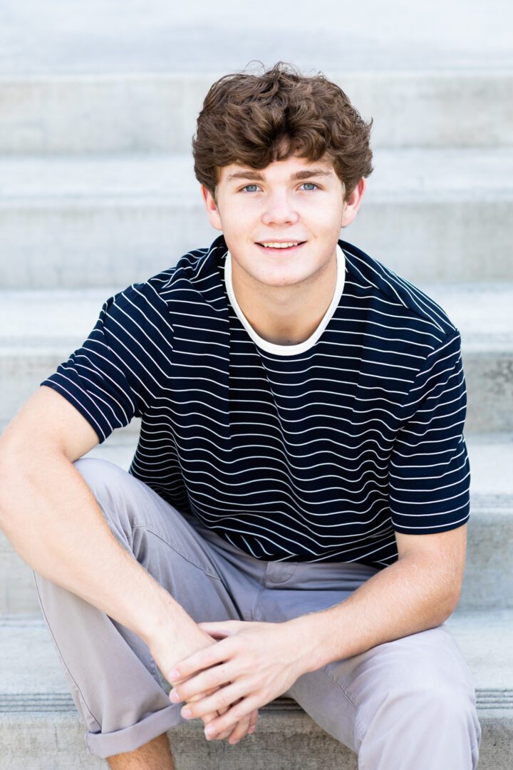 A young man sitting on some steps wearing a striped shirt.