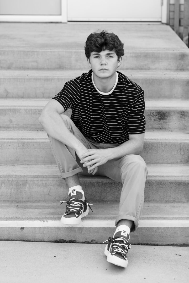 A young man sitting on some steps wearing sneakers.