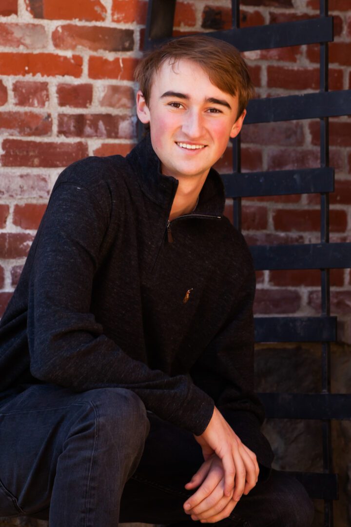A young man sitting on the ground in front of a brick wall.