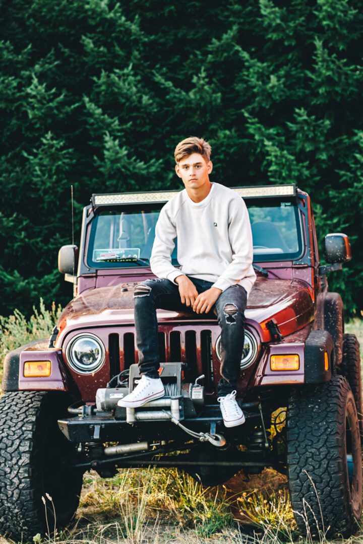 A man sitting on the hood of a jeep.