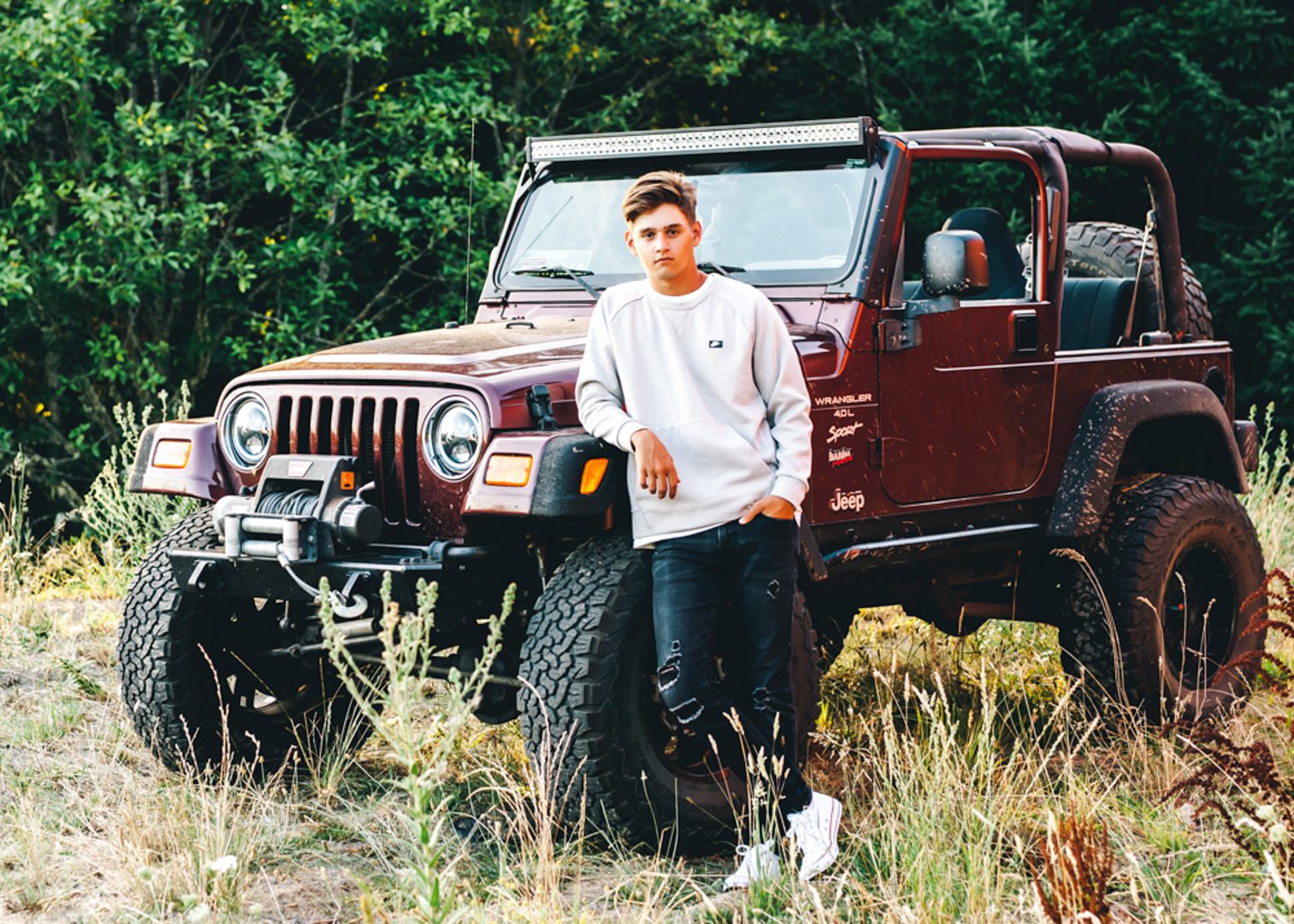 A young man standing in front of an old jeep.